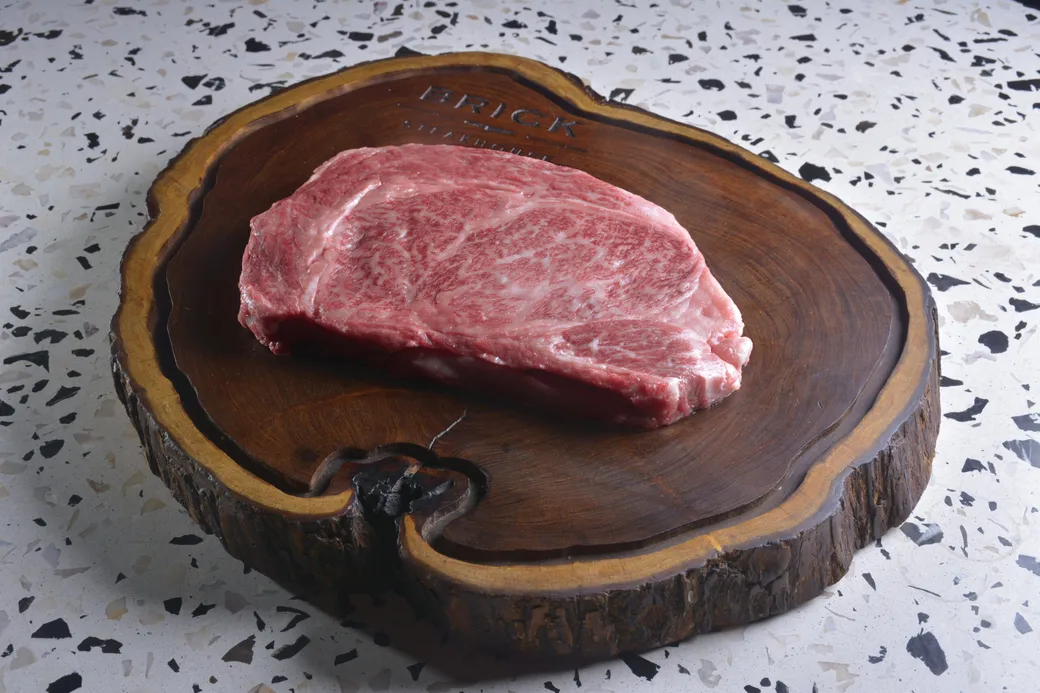 Corte wagyu crudo, muy marmoleado, sobre la tabla de madera con la marca Brick