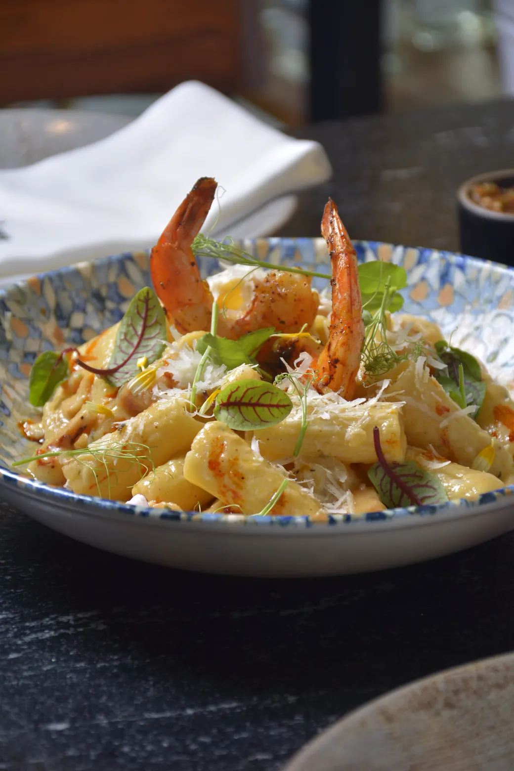 Pasta corta con camarones a la brasa, queso rallado y brotes frescos en un plato hondo azul